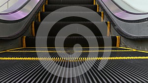 Low angle looped perspective view of modern escalator stairs. Automated elevator mechanism. Yellow line on stairway illuminated