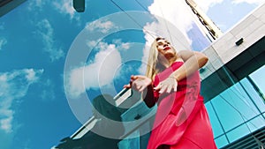 Low angle of lovely woman in red dress dancing near glass wall of skyscraper
