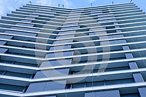 Low angle of modern facade of high rise building with glass exterior under blue sky in modern city district