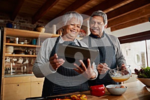 Low angle of Multi-cultural elderly couple smiling, using tablet to research recipe in modern kitchen.