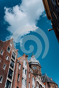 Low angle of narrow dutch houses with dome of St. Nicolas church in Amsterdam against blue sky and white cloud