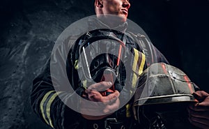 Low angle photo of a man wearing a fire suit holding an oxygen mask and helmet, looking sideways.