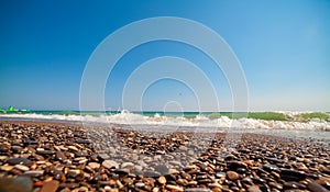Low angle photo of pebble stones on the seashore, waves and the blur sky