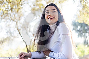 Low angle portrait of a smiling beautiful young hispanic woman sitting on park while looking camera