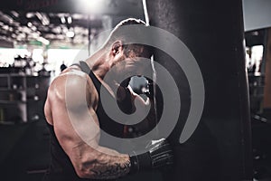 Low angle portrait of young tired sports man leaning on punching bag