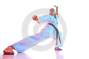 Low angle portrait of young woman, female fighter in uniform with black belt isolated over white studio background.