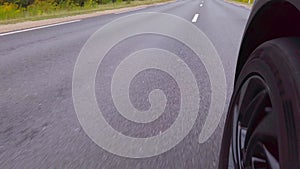 Low angle POV of front car wheel. An asphalt road with white dividing lines