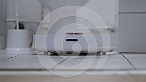 Low Angle of Robotic Vacuum Cleaner Roborock moving into close up on white tiles in a bathroom. Shot in braw. 4K