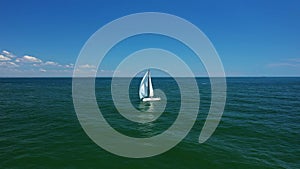 Low-angle sea-level view of small yacht boat sailing in calm open sea at sunset