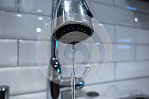 Low angle, selective macro focus on a stainless steel kitchen sink faucet, with water pouring in a thin steady stream