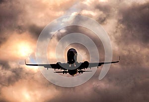 Low angle shot of an airplane flying in the dark cloudy sky at sunset