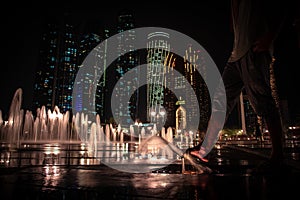 Low angle shot of a barefoot person walking on ground water fountains near Etihad Towers at night