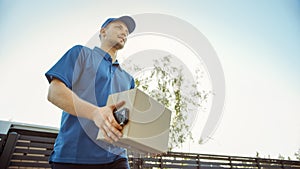 Low Angle Shot of Beautiful Young Delivery Man Delivering Cardboard Box Package. Courier Deliverin