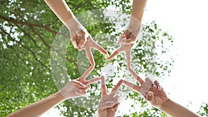 Low angle shot from below of a group of 5 young people place their hands together over sky and trees in the center of a circle.