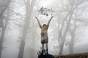 Low angle shot of a female throwing dry leaves in the air with a foggy background