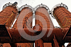 Low angle shot of four tubes of a factory with rusty railings