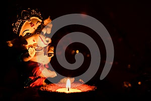 Low angle shot of Ganesha statue with a glowing lamp and a blurred dark background. Hindu festivals concept