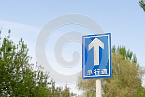 Low angle shot of a highway sign along a street on a sunny day near green trees against the blue sky