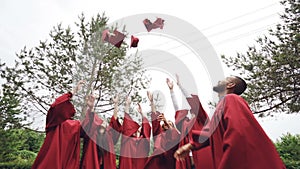 Low angle shot of joyful men and women graduating students throwing mortar-boards in the air and laughing. Beautiful