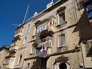 Low-angle shot of laundry hanging from building balconies against a blue sky in Malta