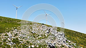 Low angle shot of a line of windmills on green hill under blue sky