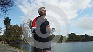 Low angle shot of a man running at park beside lake. Slow motion