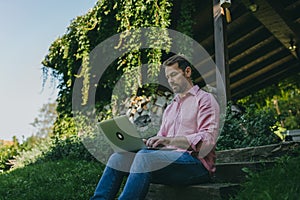 Low angle shot of man working outdoors in the garden, with laptop on legs. Businessman working remotely from homeoffice