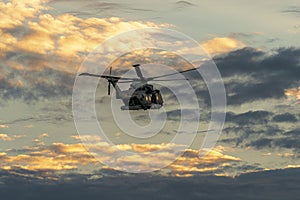 Low angle shot of a Military helicopter in a flight in the daylight cloudy sky during sunset