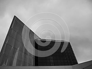 Low angle shot of a modern building with glass panels against a cloudy sky in grayscale