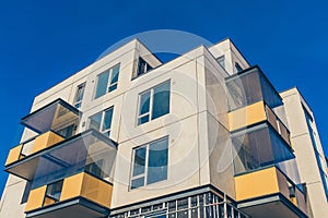 Low angle shot of a modern residential building with glass balconies and windows under the blue sky