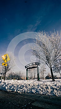 Low angle shot of a park entrance near leafless trees covered with snow under a blue sky