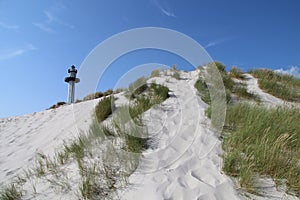 Low angle shot of a sandy hill with grasses and a lighthouse at the top in Dueodde, Bornholm