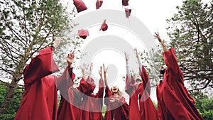 Low angle shot slow motion of happy grads throwing traditional hats in the sky, laughing and having fun on graduation