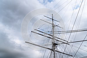 Low-angle shot of a tall ship mast and rigging on the cloudy sky background