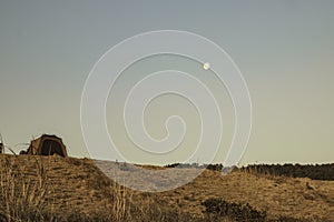 Low angle shot of a tent on a hill with a white moon in a blue sky