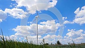Low angle shot of white wind turbine in the green field on blue cloudy sky background