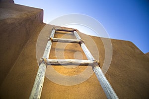 Low angle shot of a wooden ladder leaning against the wall with a clear blue sky in the background