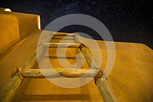 Low angle shot of a wooden ladder near the building under the dark sky full of stars