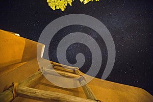 Low angle shot of a wooden ladder near the building under the dark sky full of stars