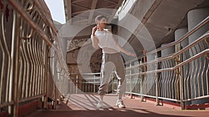 Low Angle Shot. A young cheerful guy energetically dances a street dance while standing under a city bridge outdoors. A