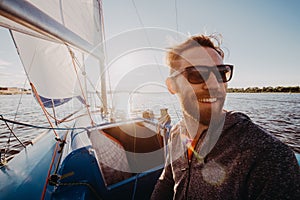 Low angle shot of a young man sailor wearing sunglasses and gloves on a sailing boat at sunset. Image toned in warm