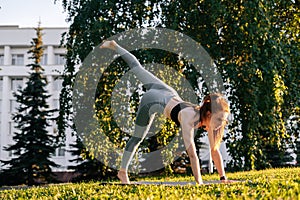 Low-angle shot of young woman practicing yoga in down facing dog pose on one leg