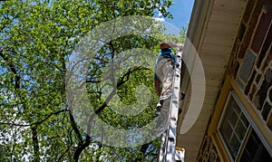 Low angle side view of man on ladder cleaning gutters of stone home