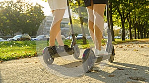 LOW ANGLE: Two unrecognizable female friends ride an e-scooter on a sunny day.