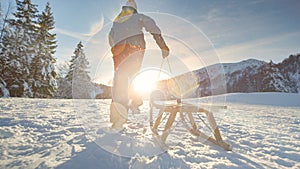 LOW ANGLE: Unrecognizable woman runs up a snowy hill with her wooden sleigh.