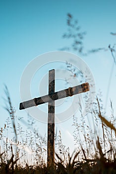 Low angle vertical shot of a hand made wooden cross in a grassy field with a blue sky in background