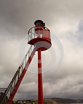 Low-angle vertical shot of a red warning beacon with ladder at harbor entrance