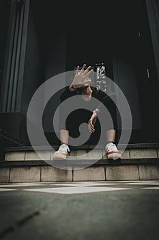 A vertical shot of a young hipster female raised her hand for dissuade while sitting on stairs