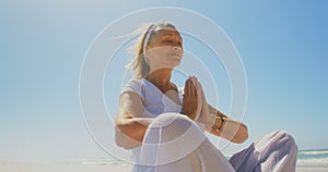 Low angle view of active senior Caucasian woman performing yoga on the beach 4k