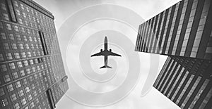 Low angle view of an airplane flying above the skyscrapers, shot in grayscale
